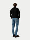 Person wearing a black turtleneck and light blue jeans on a white background.