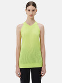 A woman wearing a sleeveless cashmere top in green, paired with black pants.#color_lime-yellow