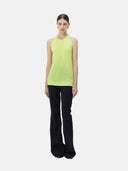A woman wearing a sleeveless cashmere top in green, paired with black pants.#color_lime-yellow