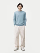 Person wearing a light blue cashmere sweater and white pants on a white background. #color_light-blue