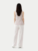 Woman wearing a light pink sleeveless cashmere top and white pants on a white background. #color_pure-white
