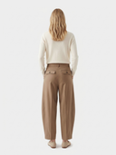 back view of a woman wearing beige pants and a white sweater on a light gray background.