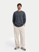 Man wearing a dark gray sweater and beige pants on a white background