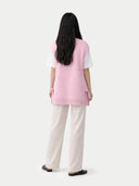 back view of a woman wearing a pink maternity top and white pants on a white background