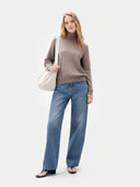 Woman wearing a brown sweater and blue jeans, holding a white bag on a white background