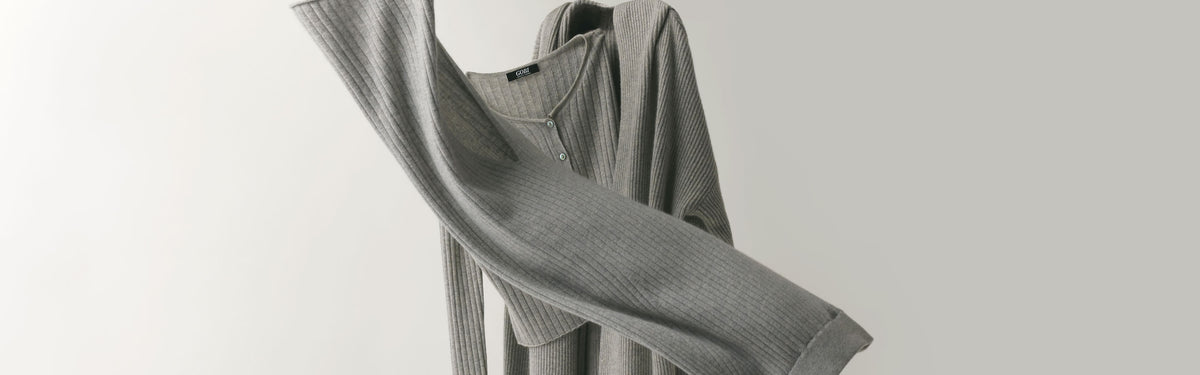 Cardigan en cachemire côtelé gris saisi en mouvement devant un mur gris clair