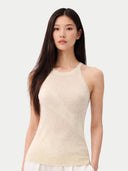 Woman wearing a beige sleeveless cashmere top and white pants on a white background. #color_off-white