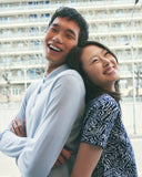 A laughing couple back to back in the city, in a pale blue cashmere polo and a navy patterned cashmere dress