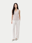 Woman wearing a light pink sleeveless cashmere top and white pants on a white background. #color_pure-white