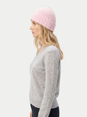 side view of a woman wearing a pink beanie and gray sweater on a white background.