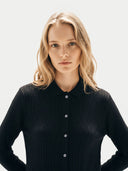Woman wearing a black ribbed sweater against a white background.