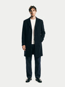 Man wearing a dark coat over a white shirt on a plain background.