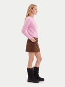 A woman shown in profile wearing a light pink ribbed knit cardigan, a brown corduroy mini skirt, and black mid-calf boots against a plain light gray studio background.