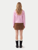 A woman viewed from behind wearing a pink cable-knit sweater, a brown mini skirt, white socks, and black ankle boots, against a light gray studio background.