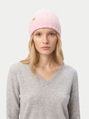 Woman wearing a pink knit beanie with a logo on a white background.