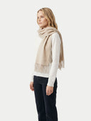 side view of a woman wearing a beige scarf with fringe on a white background.