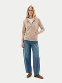 Woman wearing a beige hoodie, white shirt, blue jeans, and brown shoes on a white background