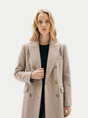 front view of a woman wearing a beige coat on a white background.