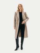 Woman wearing a beige coat and black pants on a white background.