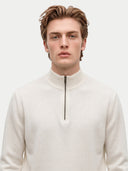 A man wearing a cream-colored quarter-zip mock neck sweater, shown from the chest up against a solid light gray background.