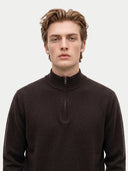 A man wearing a dark brown ribbed half-zip mock neck sweater, photographed against a clean light gray background.