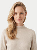 A blonde woman with wavy hair wearing a light beige knit mock neck sweater, photographed against a clean off-white background.