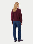 A woman with blonde hair is shown from the back wearing a maroon long-sleeve knit sweater, blue jeans, and dark loafers against a light gray studio background.