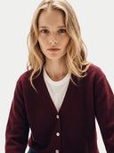 A blonde woman wearing a burgundy button-up cardigan over a white t-shirt, photographed against a clean white studio background.