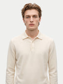 A young man with light brown hair wearing a cream-colored long-sleeve knit polo shirt, photographed against a solid light gray background.