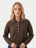 A woman with blonde hair wearing a dark brown knit polo sweater with a buttoned collar, posed against a light gray studio background.