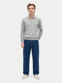 A man modeling a light gray long-sleeve polo sweater and dark blue jeans against a plain light gray studio background.