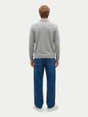 A man viewed from behind wearing a light gray long-sleeve knit polo sweater and blue jeans against a plain light gray studio background.