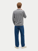A man viewed from behind wearing a heather gray long-sleeve knit sweater, blue jeans, and white sneakers against a light gray studio background.