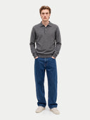 A man modeling a dark gray long-sleeve polo sweater paired with blue jeans and off-white sneakers, standing against a light gray studio background.