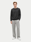 A man modeling a dark gray crewneck sweater and light gray sweatpants against a light gray studio background.