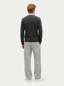 A man viewed from behind wearing a dark charcoal gray long-sleeve knit sweater and light gray sweatpants against a light gray studio background.