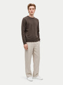 A man modeling a dark brown long-sleeve knit sweater, paired with light beige trousers and white sneakers, against a solid light gray background.