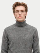 A man wearing a gray knit turtleneck sweater, photographed from the chest up against a plain light gray background.
