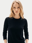 A blonde woman wearing a black long-sleeve crewneck knit sweater, photographed against a clean light gray studio background.