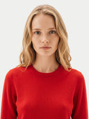 A blonde woman wearing a bright red crewneck sweater, photographed against a clean light gray studio background.