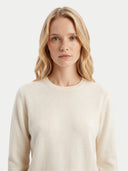 A blonde woman wearing a cream-colored crewneck knit sweater, photographed against a clean, light gray studio background.