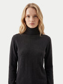 A woman with blonde hair wearing a dark charcoal gray turtleneck sweater, photographed against a clean, light gray studio background.