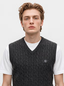 A young man wearing a dark gray cable-knit sweater vest over a white t-shirt, photographed against a clean white studio background.