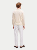 A man viewed from behind wearing a cream-colored knit polo sweater and white trousers, standing against a light gray studio background.
