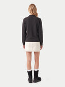 A woman is shown from the back wearing a dark charcoal gray mock neck sweater, a cream-colored mini skirt, white socks, and black ankle boots, against a light gray studio background.