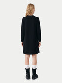 A woman viewed from the back wearing a black long-sleeve midi dress, white socks, and black ankle boots against a light gray studio background.