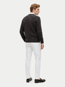 A man shown from the back wearing a dark charcoal cable-knit sweater, white trousers, and black loafers against a light gray studio background.