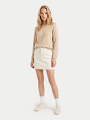 A woman modeling a beige mock-neck knit sweater and an off-white mini skirt, paired with white socks and cream sneakers, against a solid light gray background.