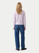 A woman viewed from behind wearing a light pink cable-knit sweater and blue jeans against a plain light gray studio background.
