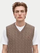 A young man wearing a light brown cable-knit sweater vest over a white t-shirt, photographed against a clean white studio background.